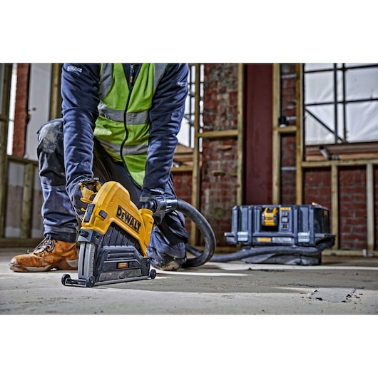 A construction worker using a DEWALT wall chaser tool to cut grooves in a concrete floor at a building site. The worker is