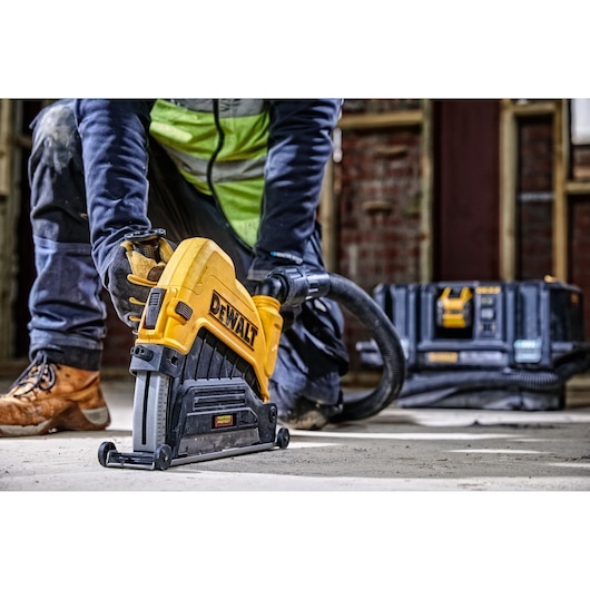 A person using a DEWALT plunge saw with a dust extraction hose attached, cutting through a concrete floor at a construction