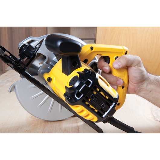 Close-up view of a person holding a DEWALT DWE560 yellow and black electric circular saw, cutting a wooden surface.