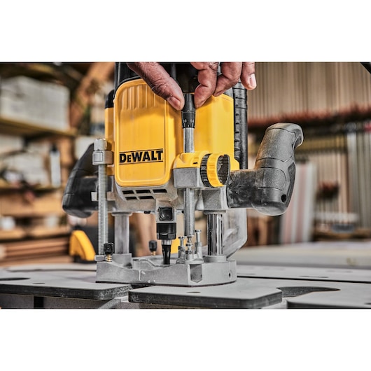 Close-up of a person adjusting a DEWALT DWE625 router tool on a workbench in a workshop setting.