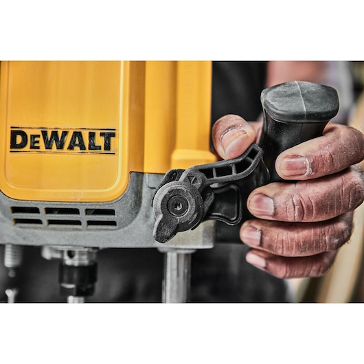Close-up of a person’s hand holding the handle of a yellow DEWALT power tool, focusing on the adjustment mechanism.