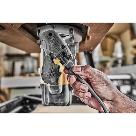 Hand connecting power cable to DEWALT tool under a workbench in a workshop.