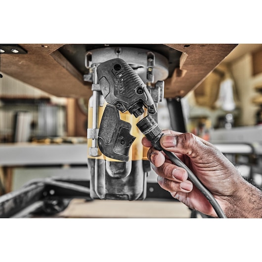 A hand connects a power cable to a DEWALT device under a worktable in a workshop setting.