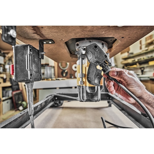 Hand plugging a cable into a DEWALT router under a workbench in a workshop.