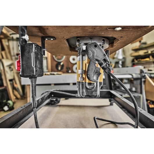 Close-up of DEWALT router DWE627KT mounted under a worktable in a workshop, with power cord and switch visible.