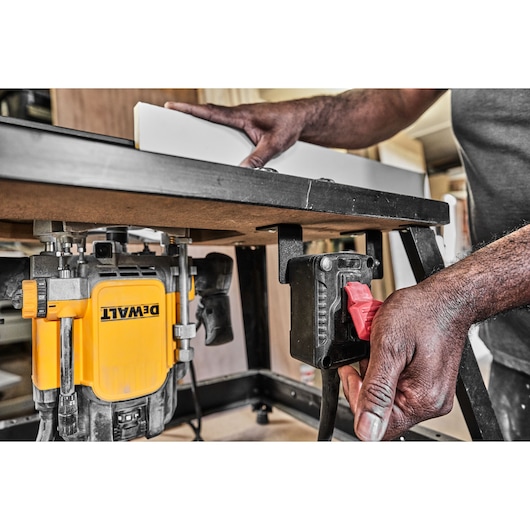 Hand operates switch on a DEWALT router table, with a board positioned for woodwork below.