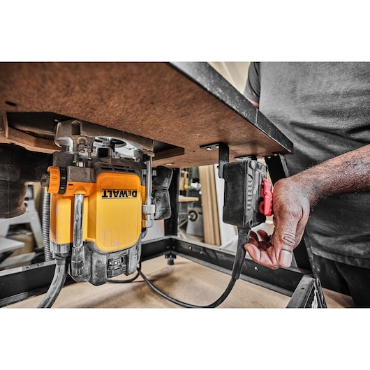 DEWALT router mounted under a worktable, a person turning on the power switch, close-up of the equipment.