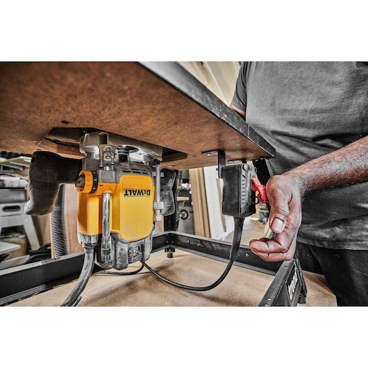 DEWALT router installed under a worktable, with a person adjusting a power switch.