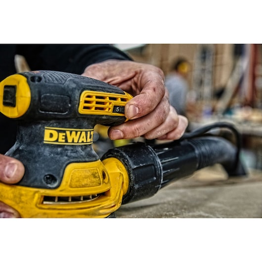 Close-up of a person adjusting a DEWALT orbital sander in a workshop setting.