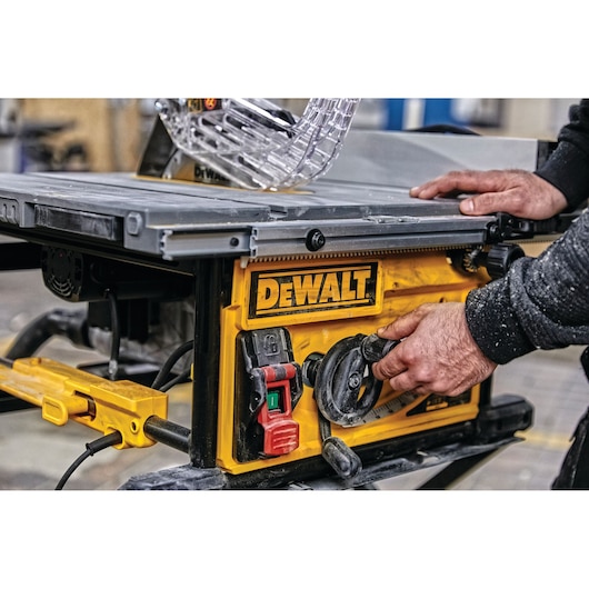 Close-up of a person adjusting the settings on a DEWALT table saw, featuring a yellow control panel with switches and dials in a workshop setting.