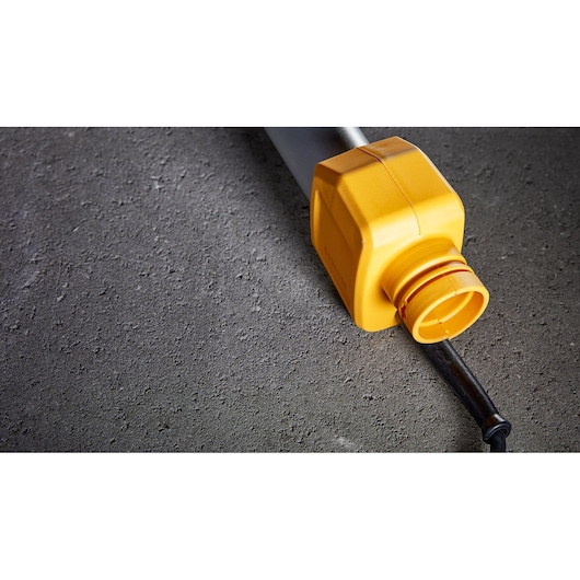 Close-up of a DEWALT power tool plug with a yellow protective cover, lying on a rough grey surface.