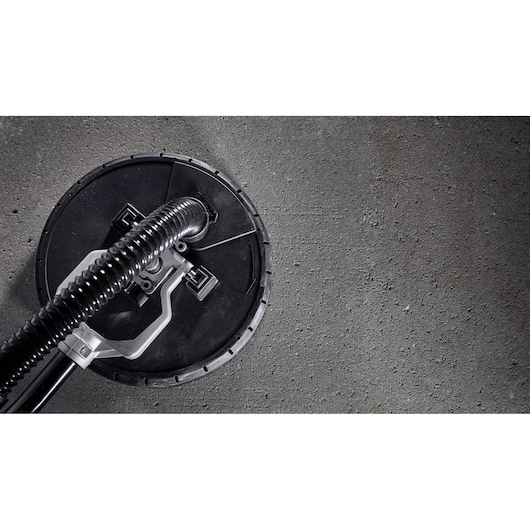 Close-up of a DEWALT DWE7800 drywall sander head with attached hose on a concrete surface.