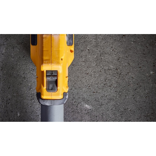 Close-up view of a DEWALT yellow power tool with a control switch, positioned against a concrete surface.
