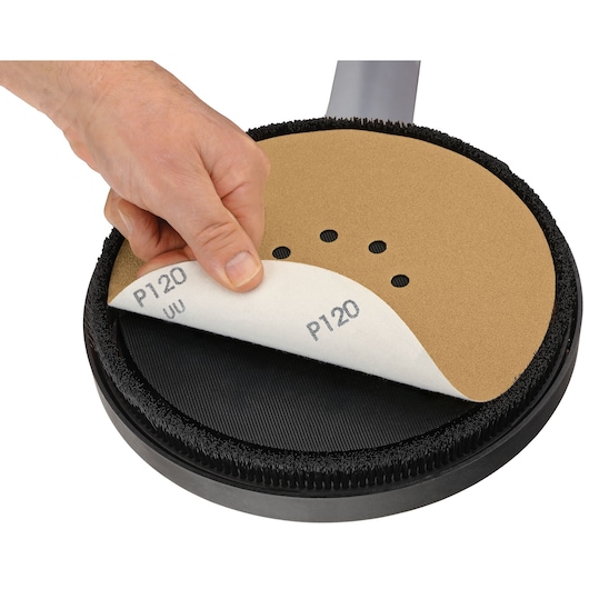 A close-up of a hand removing or attaching a P120 grit sandpaper disc to a circular power sander.
