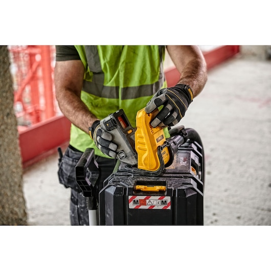 A person wearing a high-visibility vest and protective gloves is holding a DEWALT DWH079D photography tool, inserting a