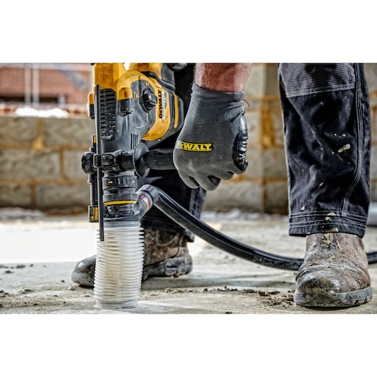 A person wearing gloves and work boots is operating a DEWALT hammer drill with a dust extraction attachment on a concrete