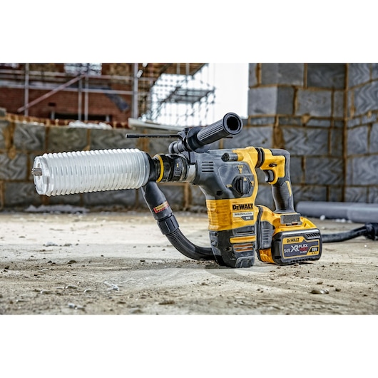 A DEWALT cordless rotary hammer drill with dust extraction attachment is positioned on a construction site, showing masonry