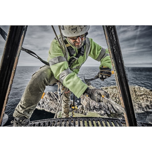 A person in safety gear and a high-visibility jacket is working outdoors at a height above the sea, using a DEWALT hammer