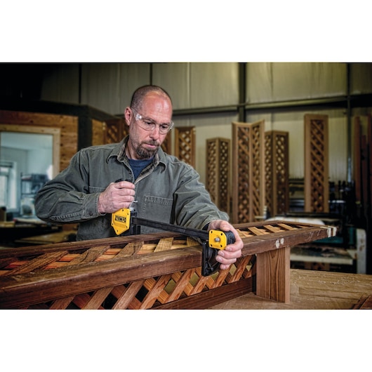 Person using a DEWALT DWHT0-83186 clamp to secure wooden lattice pieces in a workshop. The clamp is yellow and black, and