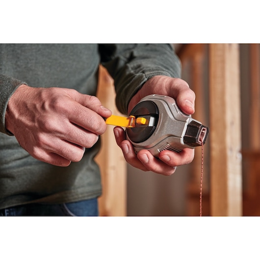 A person holding and operating a DEWALT chalk reel tool, winding the handle to retract the chalk line.