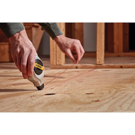 Person using a DEWALT chalk line tool to mark a straight line on a wooden surface during construction.