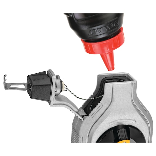 Close-up of a DEWALT chalk reel being filled with chalk powder from a bottle with a red nozzle.