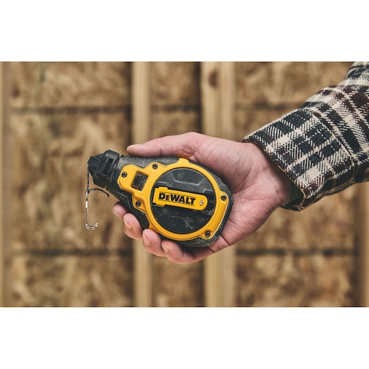 A person holding a DEWALT chalk line tool in their hand, with a construction site background.