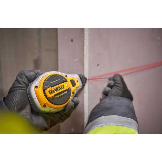 A person wearing gloves is using a DEWALT Tough Series chalk line tool, creating a red chalk line on a flat wall surface.