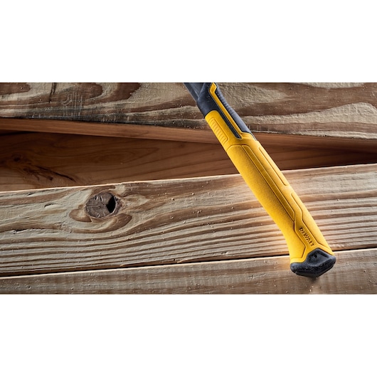A close-up of a DEWALT hammer with a yellow and black handle, lying on wooden planks.