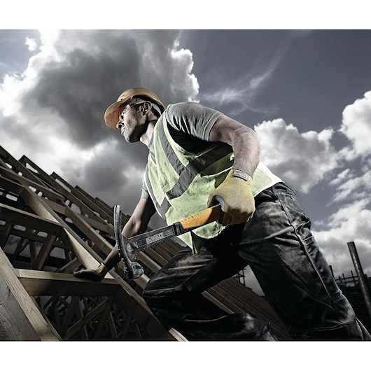 A construction worker wearing a safety helmet, high-visibility vest, and gloves is holding a DEWALT hammer (DWHT51145-0)