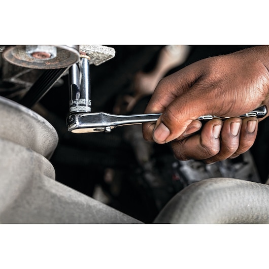 A close-up of a hand using a DEWALT ratchet wrench to tighten or loosen a bolt on a machine or engine.