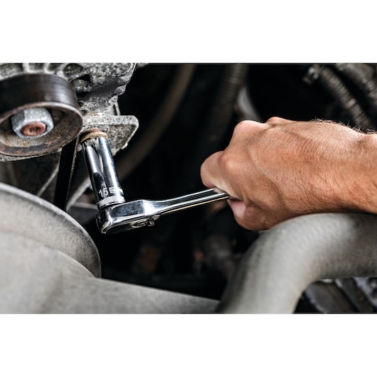 A close-up of a hand using a chrome ratchet wrench with a 15 mm socket to tighten or loosen a bolt in a mechanical or