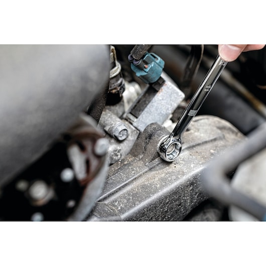 A hand uses a DEWALT ratcheting wrench to tighten a bolt on a dusty engine part.