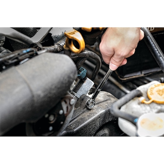 Hand uses DEWALT wrench to tighten bolt in car engine compartment.