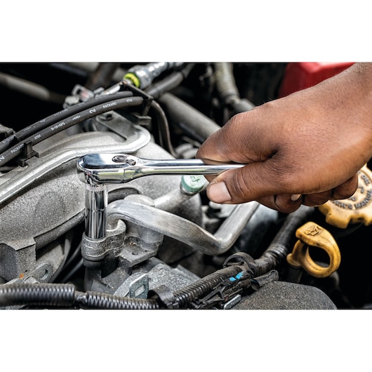 Hand using a DEWALT ratchet wrench on a bolt inside a car engine compartment.