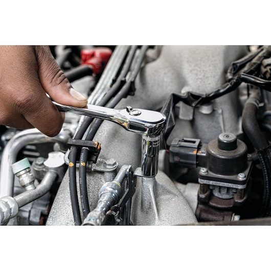 Hand using a DEWALT ratchet on a bolt in a car engine compartment.