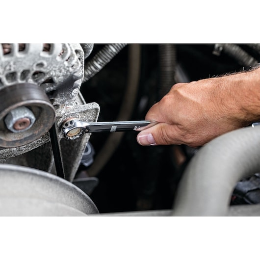 Hand using a DEWALT wrench to tighten a bolt on a mechanical engine part.