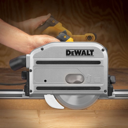 A close-up image of a DEWALT DWS520K track saw being operated by a person's hand, cutting through a piece of wood. The saw is silver with black and yellow accents and features the DEWALT logo prominently on the side.