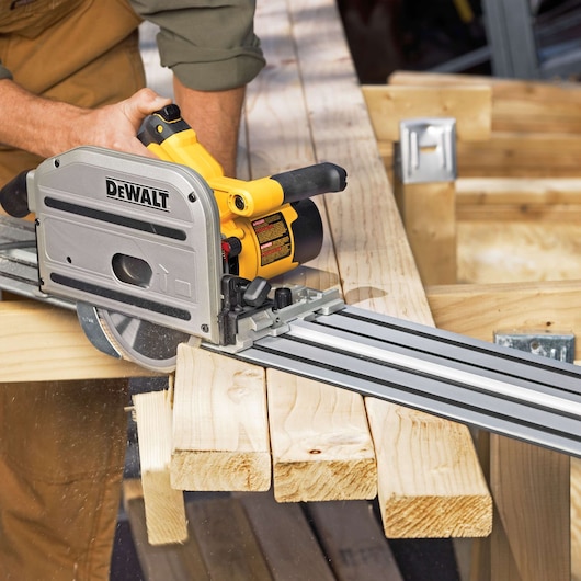 A person using a DEWALT track saw to cut wooden boards, with the saw guided along a metal track for precise straight cutting.