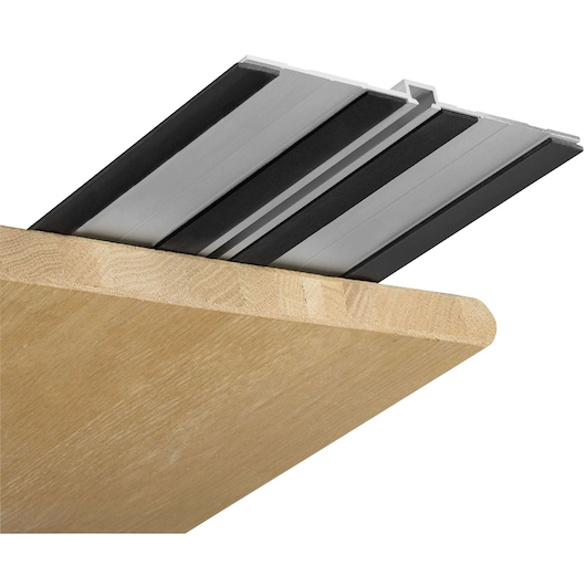 Close-up of a DEWALT track saw guide rail attached to the edge of a wooden board, showing the metal track and black rubber strips.