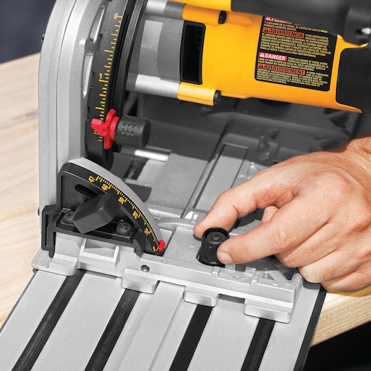 Close-up of a person adjusting the settings on a DEWALT DWS520K track saw, showing the saw’s adjustment knobs and measurement guides.