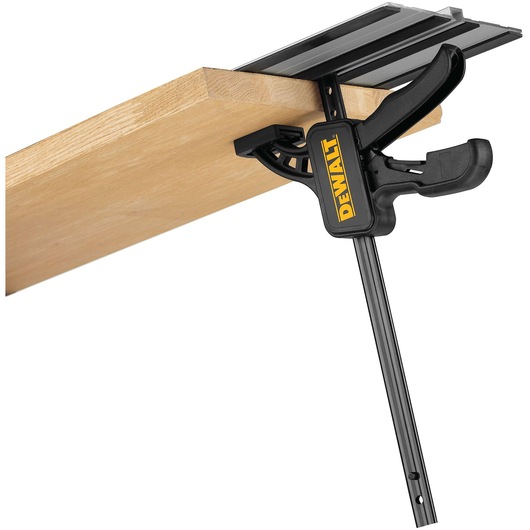A DEWALT branded clamp attached to a wooden board, designed for securing materials during cutting or assembly tasks.