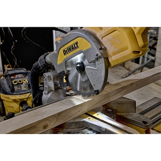 DEWALT miter saw cutting a wooden plank in a workshop setting.