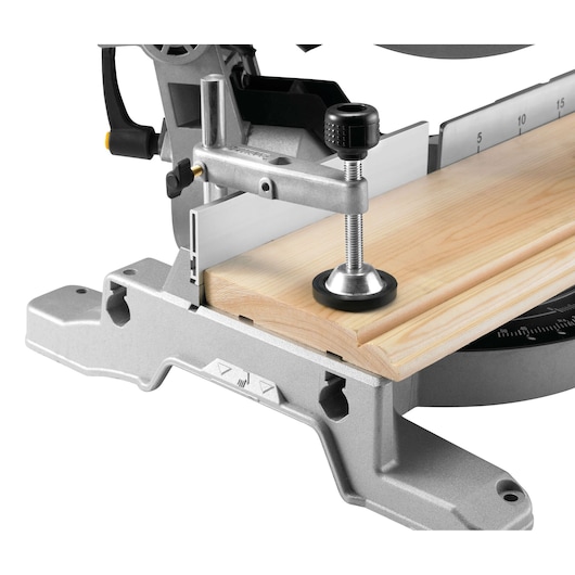Close-up of a DEWALT mitre saw holding a wood piece with a clamp on its cutting base.