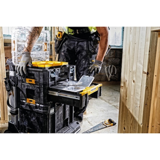A person wearing work gloves and construction attire is organizing tools in a DEWALT DWST1-70705 stackable toolbox system