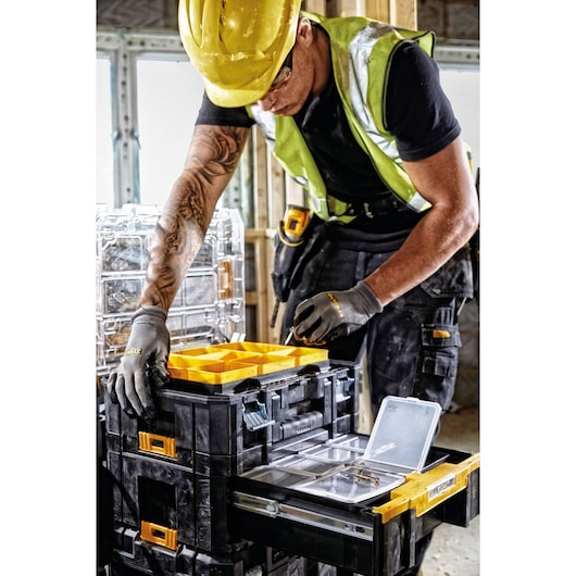 A construction worker wearing a yellow hard hat and safety vest is organizing tools and components in a DEWALT DWST1-70705