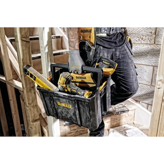 A DEWALT black and yellow tool box being carried by a person wearing work gloves and utility pants. The box contains various