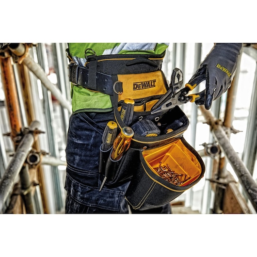Close-up of a DEWALT tool belt worn by a person on a construction site, showing various hand tools and a pouch filled with