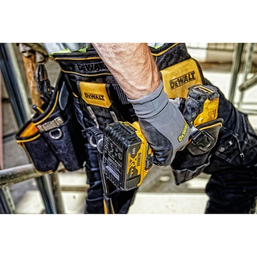 Close-up of a person wearing a DEWALT tool belt and gloves, holding a cordless power tool. The tool belt has multiple