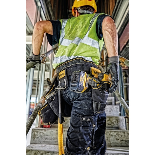 A construction worker wearing a yellow safety helmet, a high-visibility green vest, and gloves is ascending a concrete